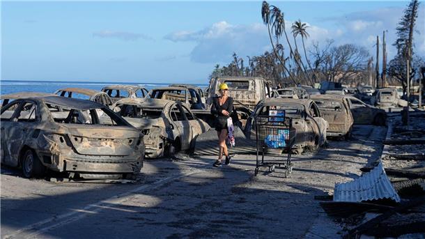 Nach tödlichen Bränden auf Maui: Klage gegen Stromversorger  Eine Frau geht an zurückgebliebenen Trümmern nach dem Waldbrand in Lahaina vorbei.