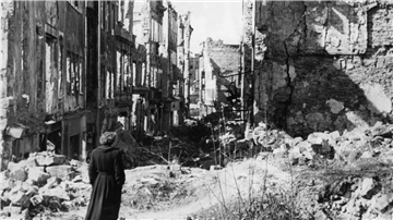 Eine Frau geht in einer Straße in Dresden an Häusern vorbei, von denen nach dem Zweiten Weltkrieg nur noch Ruinen geblieben sind.