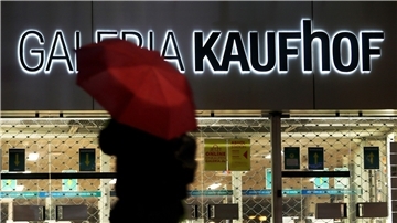 Eine Frau geht mit Regenschirm an einer geschlossenen Kaufhof Filiale vorbei.