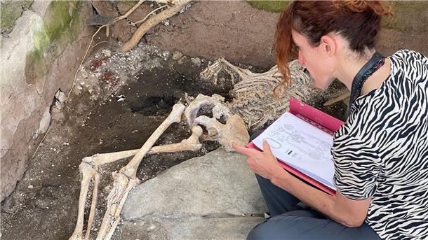 Drei Skelette in versunkener Römer-Stadt Pompeji entdeckt Eine Frau sitzt vor einem Skelett im Archäologiepark Pompeji.