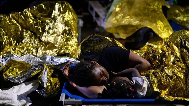 Tausende Migranten auf Lampedusa: Anspannung und Erschöpfung Eine Frau und ein Kind sowie weitere Menschen schlafen im Freien vor dem Erstaufnahmelager auf Lampedusa.