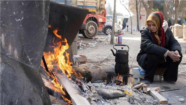 Hoffnung und Trauer: Erschöpfte Helfende in der Türkei Eine Frau wärmt sich auf offener Straße in Kahramanmaras an einem Feuer auf.
