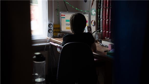 Eine Jugendliche sitzt in einem abgedunkelten Zimmer vor ihrem PC beim Homeschooling.