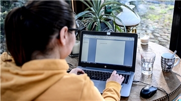 Eine junge Frau arbeitet im Homeoffice in einem Wintergarten.