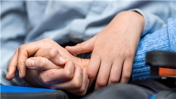 Eine Mutter hält die Hand ihres Kindes, das im Rollstuhl sitzt. Nahaufnahme der Hände.