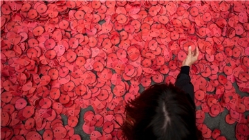 Eine Person hebt eine Papiermohnblume auf, die während einer Kundgebung gegen den Gaza-Krieg vor dem spanischen Außenministerium in Madrid auf dem Boden liegt. 