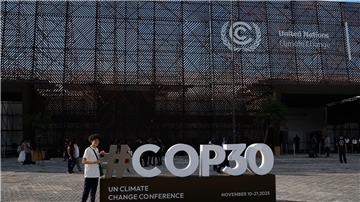 Eine Person posiert für ein Foto mit einem Schild für den UN-Klimagipfel COP30. 