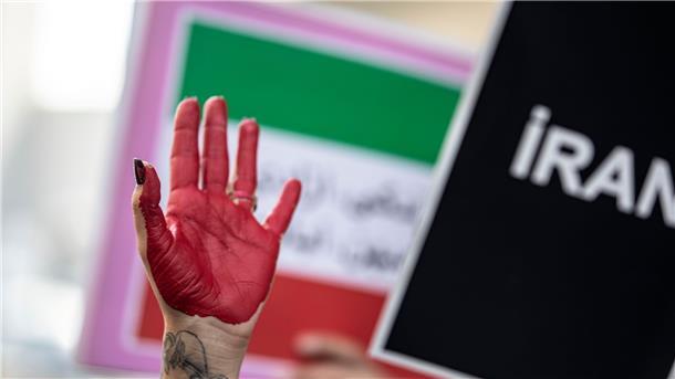 Iran richtet erstmals seit Protestbeginn Demonstranten hin Eine rot bemalte Hand einer Frau erhebt sich zwischen Plakaten während einer Demonstration.