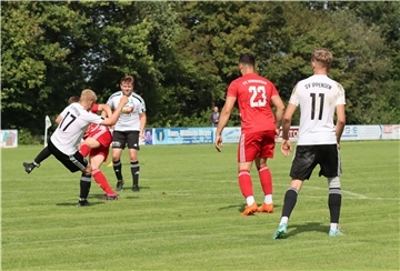 Drei Männer in schwarz-weißen Trikots und zwei in roten Trikots haben einen Fußball im Blick.