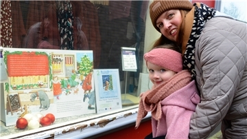 Mareike Buck und ihre Tochter Aenne lesen beim Bilderbuch-Spaziergang die erste Seite der Weihnachtsgeschichte in einem Schaufenster  