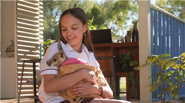 Ein Mädchen hält ein Känguru-Baby auf dem Arm. Lilly (Lily Whiteley) kümmert sich rührend um Känguru-Kinder, die keine Mutter mehr haben.