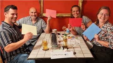 Vier Erwachsene - zwei Männer (links) und zwe iFrauen - sitzen an einem Tisch und halten farbige Umschläge in den Händen. Elf Teams traten beim ersten Gezeiten-Pub-Quiz auf Hof Iggewarden gegeneinander an. Das Foto zeigt das Gewinnerteam „Die Poustourlis".