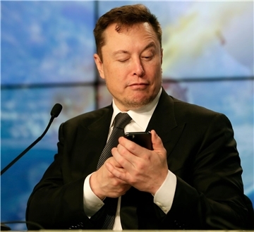 Elon Musk schaut auf sein Handy.