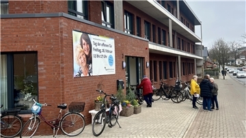 Viele Fahrräder Parken vor einem Neubau, eine Gruppe von fünf Menschen steht davor.