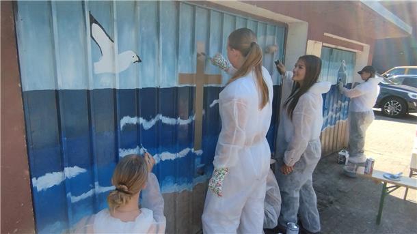 Einige junge Frauen in weißen Overalls malen auf zwei Garagentore.
