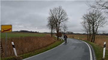Ein Mann fährt mit seinem Fahrrad auf einer schmalen Kreisstraße.