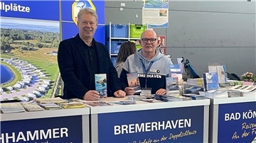 Zwei Männer halten Prospekte in die Kamera.