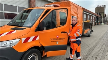 Ein Mann neben einem orangefarbenen Auto. Erdmann Wittje ist seit 50 Jahren bei der Straßenmeisterei tätig.  