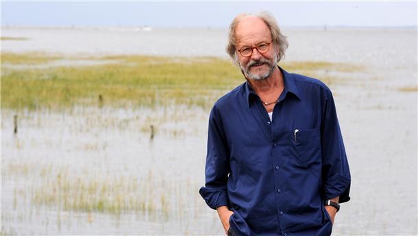 Mann steht vor überschwemmter Wiese, im Hintergrund ist die Nordsee zu sehen