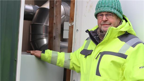 Ernst Schnackenberg von der Firma Schnackenberg GmbH steht vor einem Schalterschrank einer Power-to-Heat-Anlage. Eine Art riesiger Tauchsieder erhitzt Wasser in einem Speicher. Auch wenn er seinen Strom bei einer Netzüberlastung nicht mehr ins Netz einspeisen darf, ist die Wärmeversorgung der angeschlossenen Haushalte gesichert.