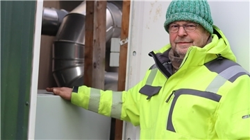 Ernst Schnackenberg von der Firma Schnackenberg GmbH steht vor einem Schalterschrank einer Power-to-Heat-Anlage. Eine Art riesiger Tauchsieder erhitzt Wasser in einem Speicher. Auch wenn er seinen Strom bei einer Netzüberlastung nicht mehr ins Netz einspeisen darf, ist die Wärmeversorgung der angeschlossenen Haushalte gesichert.