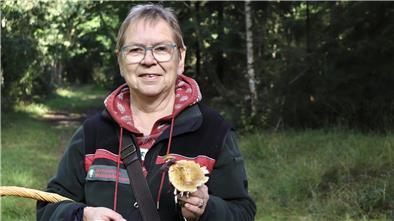 Eine Frau hält einen Pilz in der Hand und blickt in die Kamera.