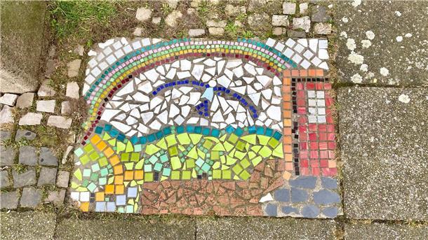 Es leuchtet im tristen aschgrauen Gehwegpflaster: Das farbensprühende Mosaik im Bremerhavener Scharnhorst-Viertel hat eine Anwohnerin im Gedenken an ihren geliebten Mann dort in den Boden eingebaut.