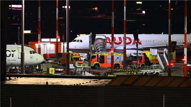 Fahrzeuge der Feuerwehr und ein Krankenwagen stehen am Flughafen vor einem Flugzeug.