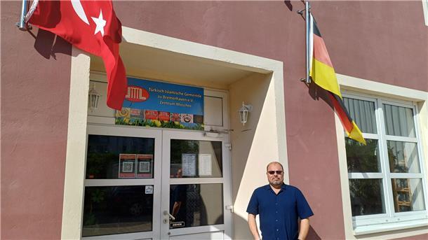 Ein Mann vor einem Eingang mit deutscher und türkischer Flagge.