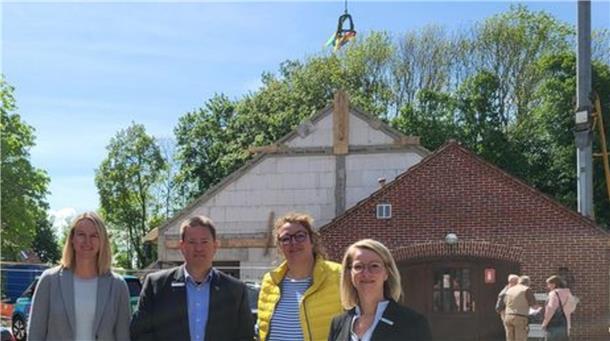 Vier Menschen vor einem Neubau mit Richtkrone