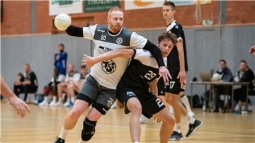 Zwei Männer in schwarz-weißen Trikots kämpfen um einen kleinen Ball.
