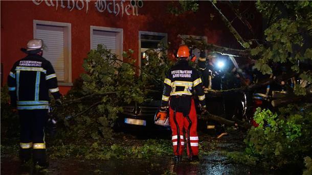Verletzte nach heftigen Unwettern im Süden und Westen Feuerwehrleute beseitigen einen Baum, der im baden-württembergischen Ravensburg auf ein Auto gestürzt ist.