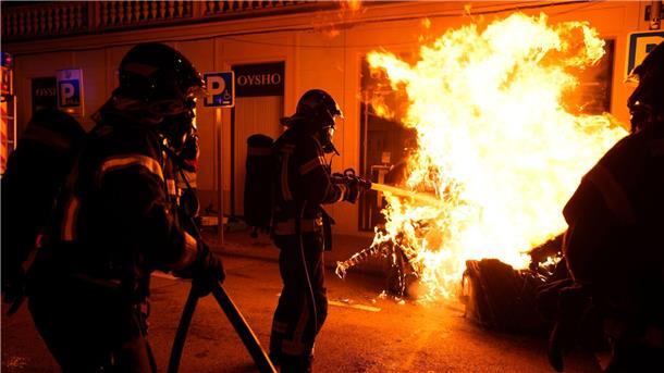 Feuerwehrleute müssen einen von Demonstranten angezündeten Müllcontainer löschen.