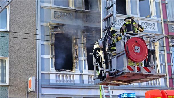 Feuerwehrmänner stehen vor dem Mehrfamilienhaus in Solingen; Rauch dringt aus einem der Fenster.