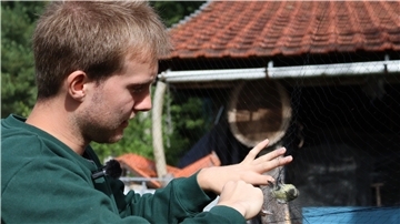 Mann im grünen Pullover vor Vogelfangnetz