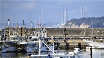 Fischerboote im Hafen von Namie vor dem Hintergrund des havarierten Kernkraftwerks Fukushima Daiichi.