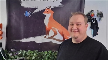 Florian Haase vor einem Plakat seines Spiels „Paws and Leaves“.