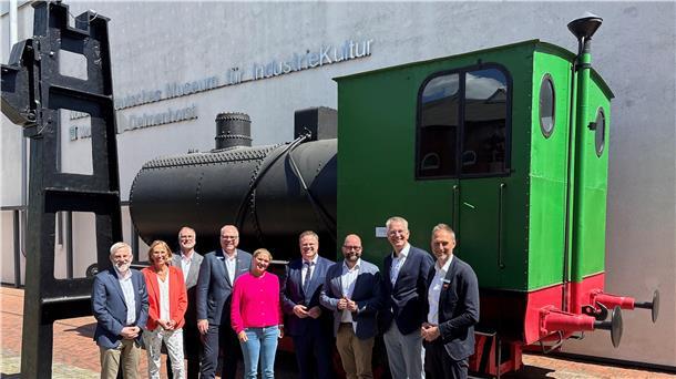 Eine Gruppe von Erwachsenen stehen vor einer alten Lokomotive.