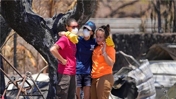 Frauen umarmen sich in den Trümmern eines vom Feuer zerstörten Hauses in Lahaina auf Hawaii.