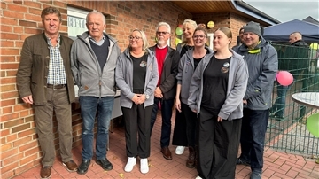 Gruppenfoto vor dem Gebäude der Freizeitstätte Wremen: Mitarbeitende und Gäste, darunter Vertreter der Gemeinde, stehen lächelnd nebeneinander. Im Hintergrund sind Luftballons und ein Zelt-Pavillon zu sehen.