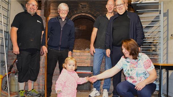 Vier Männer, eine Frau und ein Kind stehen vor einem Steinbackofen.