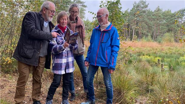 Vier Menschen stehen in einer Moorlandschaft und betrachten ein Buch. 