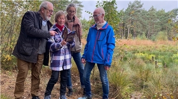 Vier Menschen stehen in einer Moorlandschaft und betrachten ein Buch. 