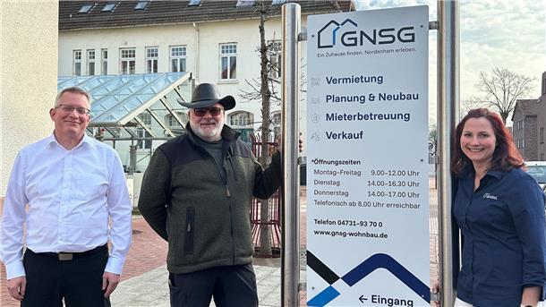 Zwei Männer und eine Frau stehen vor dem Sitz der Gemeinnützigen Nordenhamer Siedlungsgesellschaft (GNSG).