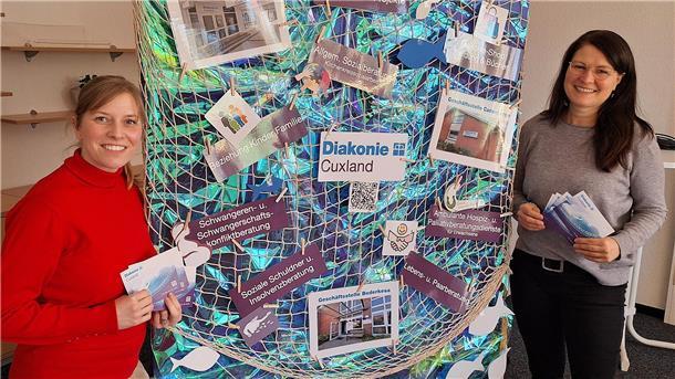 Angebot der Diakonie: „Schwangeren-Treff“ und Gruppe „Unerfüllter Kinderwunsch“ Zwei Frauen haben Broschüren in der Hand. Sie stehen neben einem aufgehängten Fischernetz. Im Netz sind Info-Materialien deponiert.