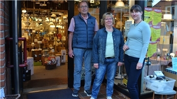 Zwei Frauen und ein Mann stehen neben einer geöffneten Tür. Im Hintergrund sind Leuchten zu sehen.