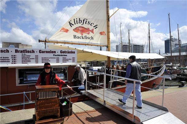 Der perfekte Tag in Bremerhaven für Sie und Ihren Hund Ein kleines Schiff mit Segel am liegt am Neuen Hafen in Bremerhaven. Auf dem Segel steht Klibfisch, Backfisch.