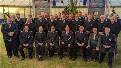 Gruppenfoto der Freiwilligen Feuerwehr Kirchwistedt anlässlich des 105-jährigen Jubiläums. Etwa 30 Feuerwehrmitglieder in Uniform sowie einige ältere Herren sitzen und stehen in mehreren Reihen in einem Festzelt. Im Hintergrund sind Bühnenelemente und Banner der Veranstaltungstechnik „Sound & Light Ringstedt“ zu sehen.