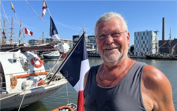Ein Mann vor einem Schiff mit französischer Flagge.