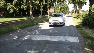 Ein silberner Pkw fährt auf einer schmalen Landstraße über eine neu installierte Fahrbahnschwelle in der Alten Lindenstraße in Dorfhagen.